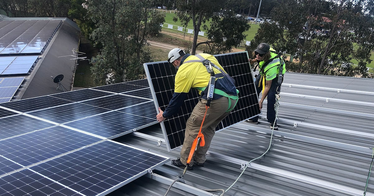 Two men istalling solar panels on the roof of the Sapphire Aquatic Centre