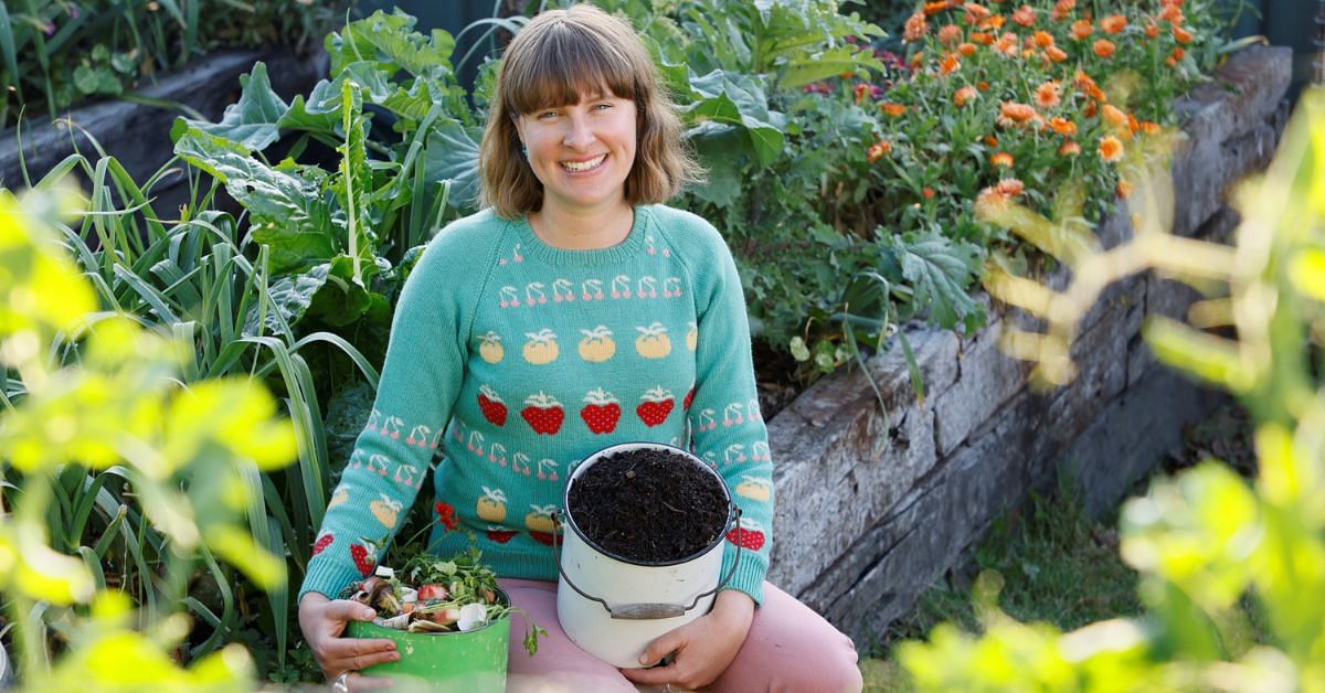 Composting guru, Kate Flood sitting in a veggie garden holding a bucket of compost