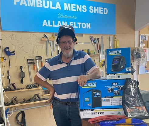 A man with a beard and a helmet perched on his head stands with boxes of welding gear.