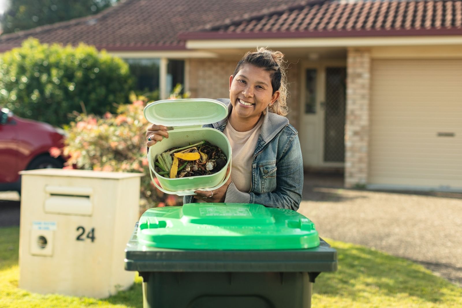 A woman holding a full FOGO caddy bin above a green lid food and organics bin