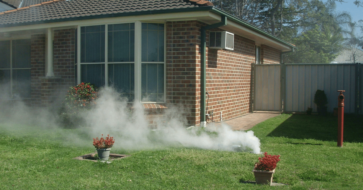 Smoke coming from the ground on the lawn of a suburban brick house