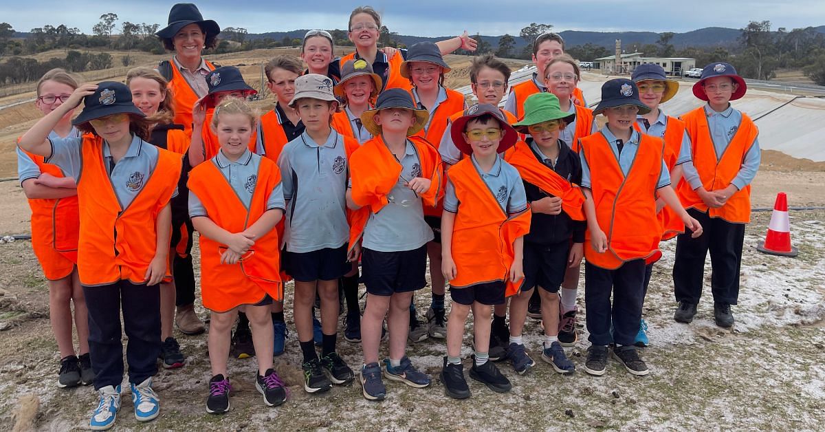 19 Pambula Public School students with a teacher standing in a landfill cell in a group photo shot