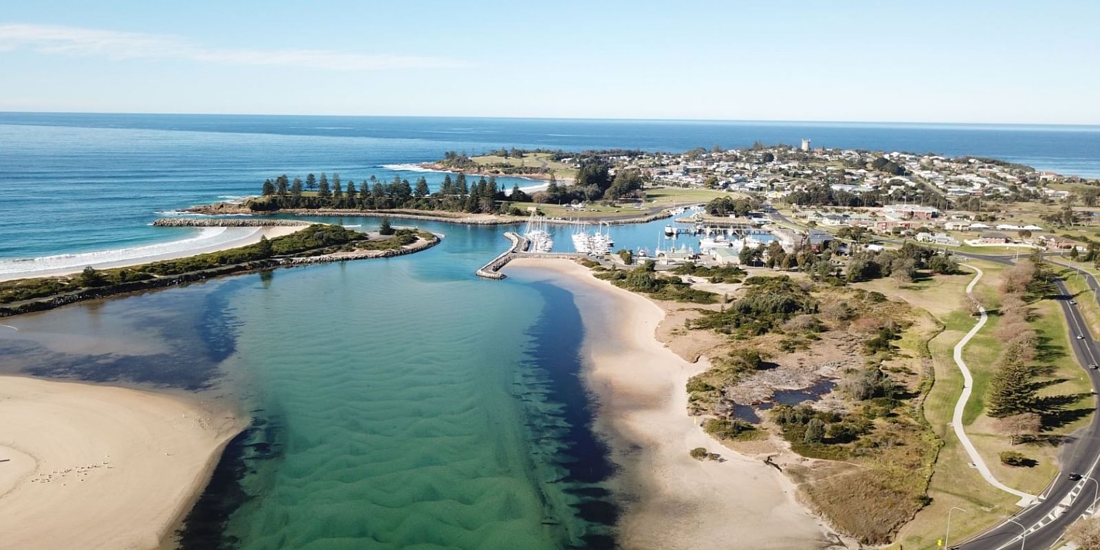 An aerial view of a town situated on a harbour, river mouth and coastline intersected by a bridge