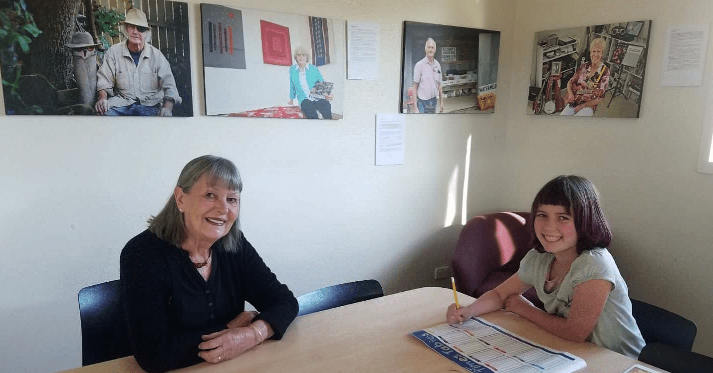 A woman seated at a table helps to supervise a young girl's homework