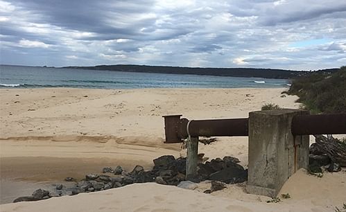 A cloudy sky over a beach showing an ocean outfall pipe in the foreground.