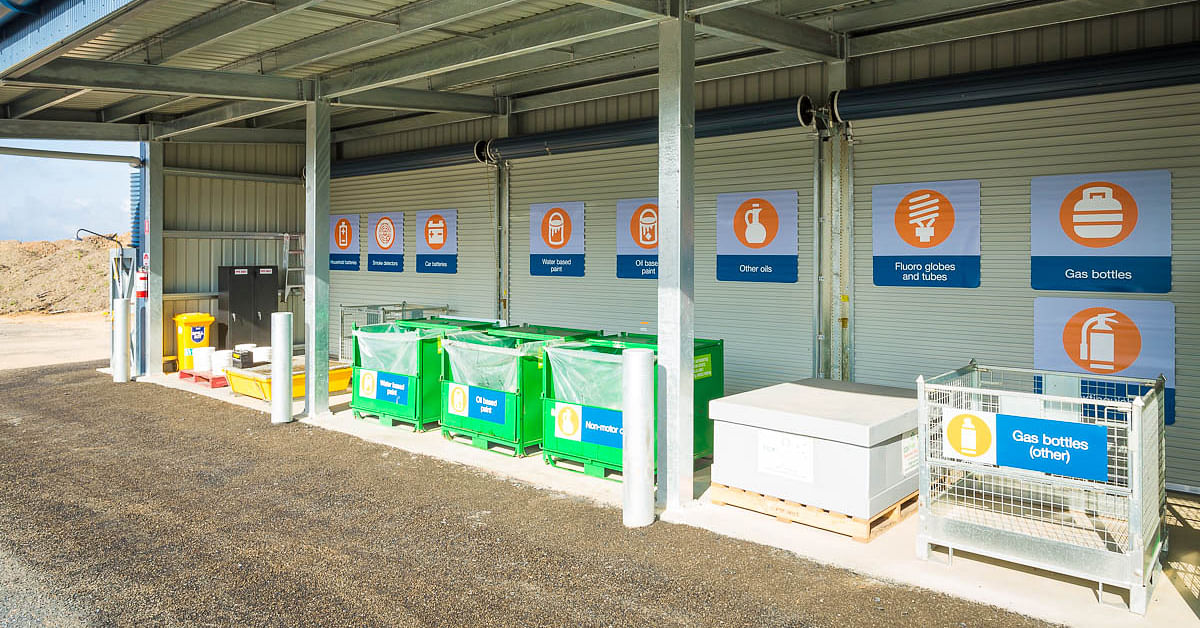 Community recycling centre with bins in a line an signs above each bin.